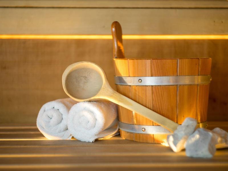 Dřevěné vědro, naběračka a srolované ručníky v sauně s teplým osvětlením