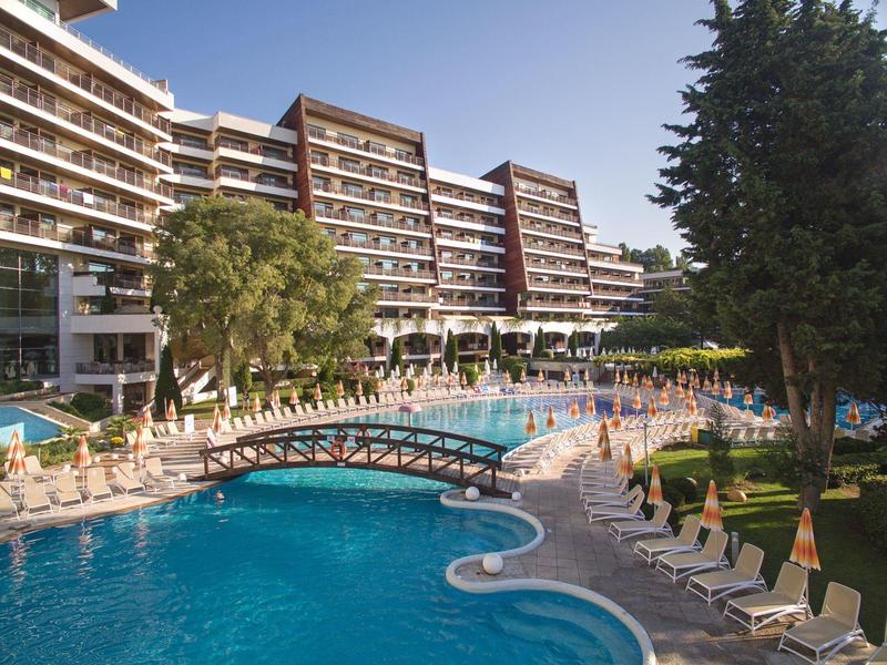 Velký vícepatrový hotel s bazénem, mostem a lehátky venku.