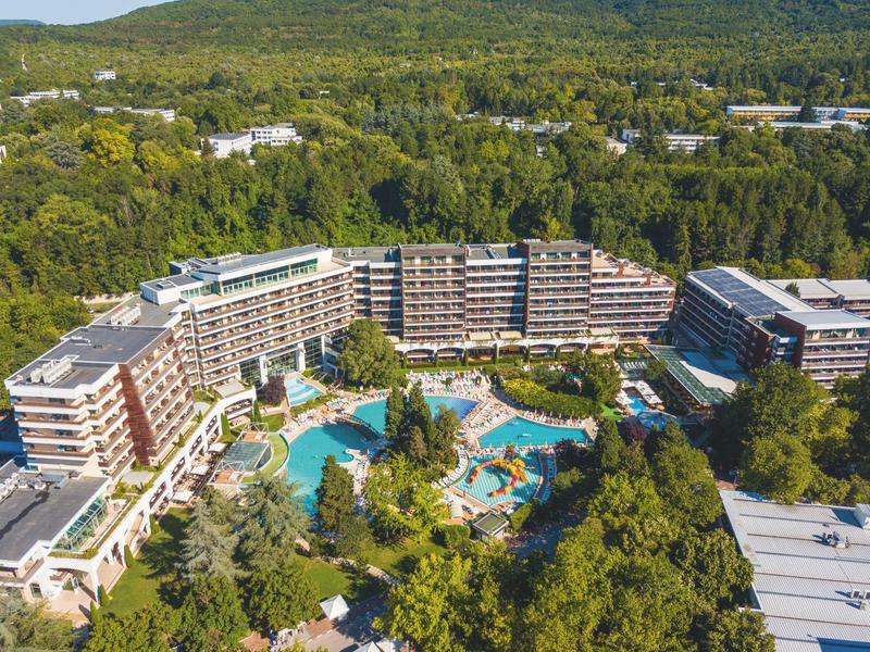 Velký hotelový resort s zakřiveným bazénem obklopený hustým lesem.