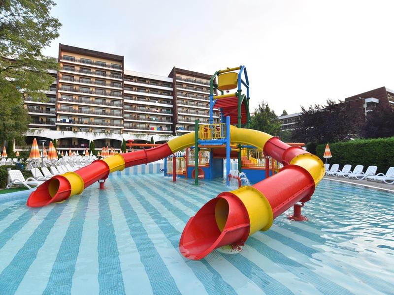 Dětská vodní skluzavka se žlutými a červenými trubkami v bazénu před hotelem