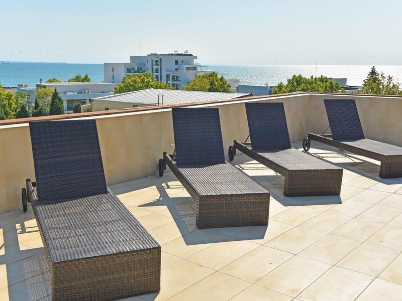 Několik lehátek na slunné terase s výhledem na moře a budovy.
