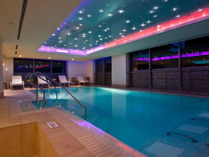 Moderní vnitřní bazén s osvětlením stropu a lehátky v hotelu.