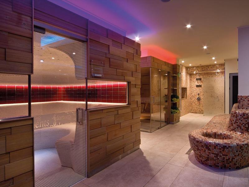 Moderní wellness prostor s dřevěnou saunou, barevným osvětlením a pohodlným křeslem.