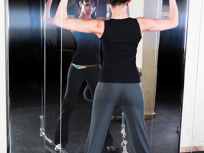 Žena cvičí na posilovacím stroji před zrcadlem uvnitř.