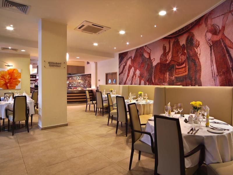 Elegantní hotelová restaurace s kulatými stoly, pohodlnými židlemi a velkou nástěnnou malbou.