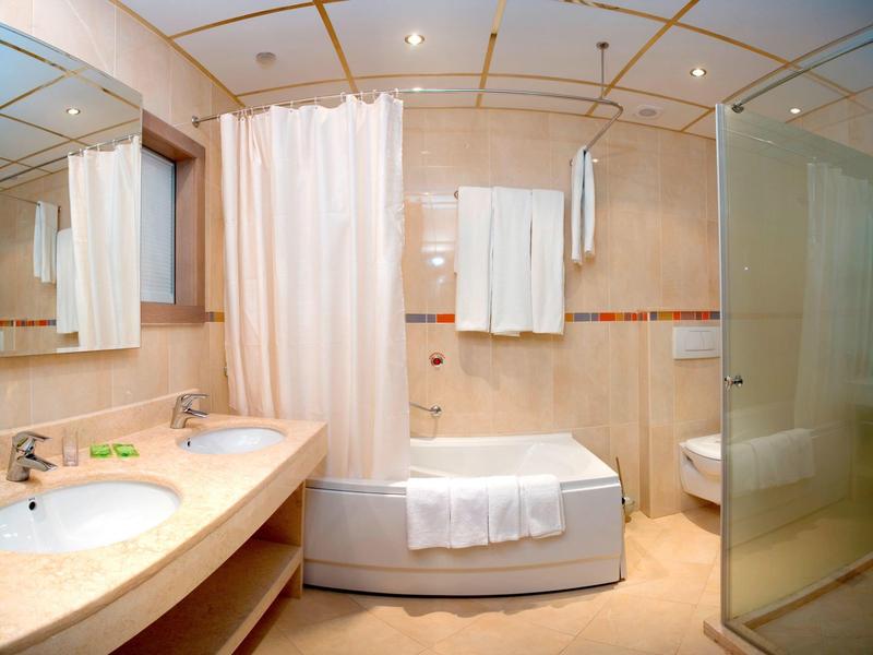 Světla koupelna s dvojitým umyvadlem, vanou, sprchou a ručníky v hotelu.