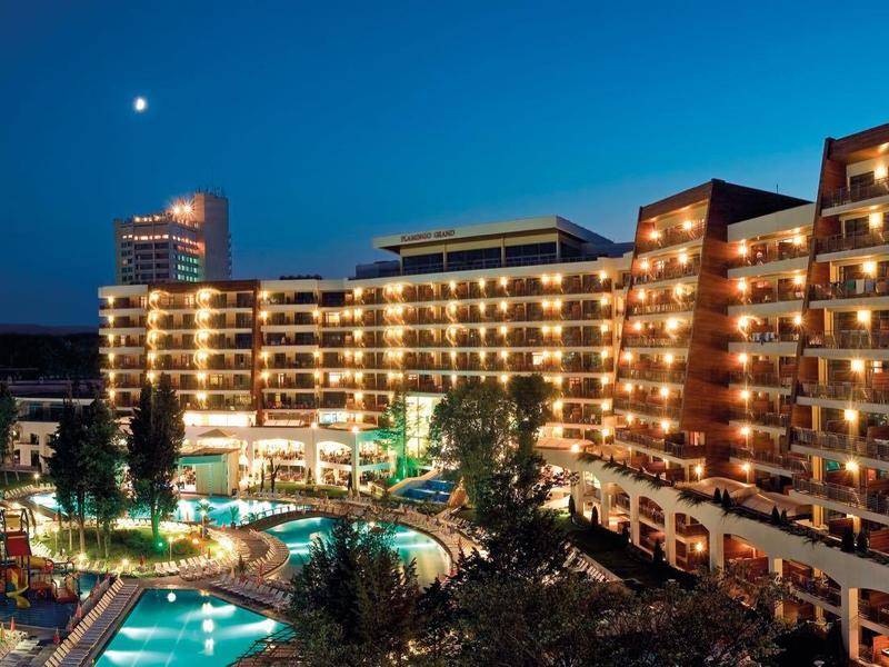 Noční pohled na osvětlené letovisko s bazénem a horami v pozadí.