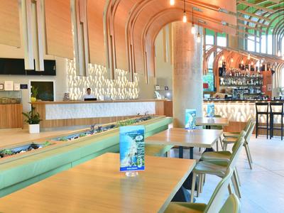 Restaurant moderne avec de longues tables en bois, des chaises vertes et un intérieur lumineux et aéré.