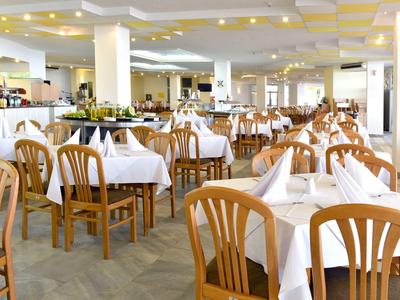 Grande salle à manger avec de nombreuses tables en bois et nappes blanches, prête pour les invités.