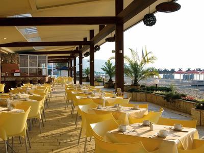 Balkon z białymi krzesłami i szklanymi drzwiami z widokiem na zielony krajobraz i niebieskie niebo.