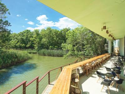 Balcon avec des sièges le long d'une rivière, entouré d'arbres sous un ciel clair.