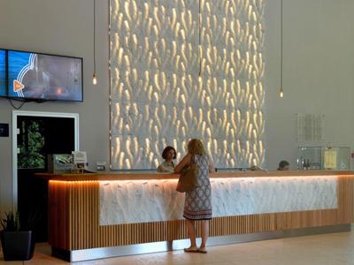 Nowoczesna recepcja hotelowa z jasnym drewnem, ławką i dwoma ekranami na ścianie