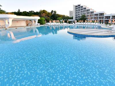 Grande piscine d'hôtel avec eau bleue, chaises longues et bâtiment d'hôtel moderne en arrière-plan