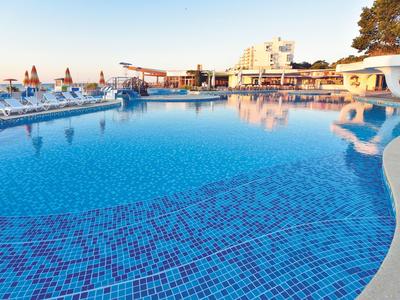 Duży basen z czystą niebieską wodą i leżakami w hotelu o zachodzie słońca.