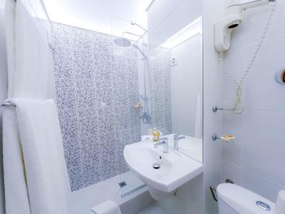 Mała, nowoczesna łazienka hotelowa z prysznicem, umywalką, lustrem i suszarką na ścianie.