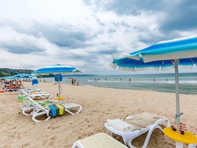 Pusta plaża z leżakami i niebieskimi parasolami pod pochmurnym niebem