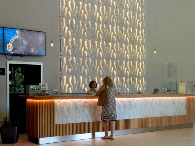 Nowoczesna recepcja hotelowa z jasnym drewnem, ławką i dwoma ekranami na ścianie