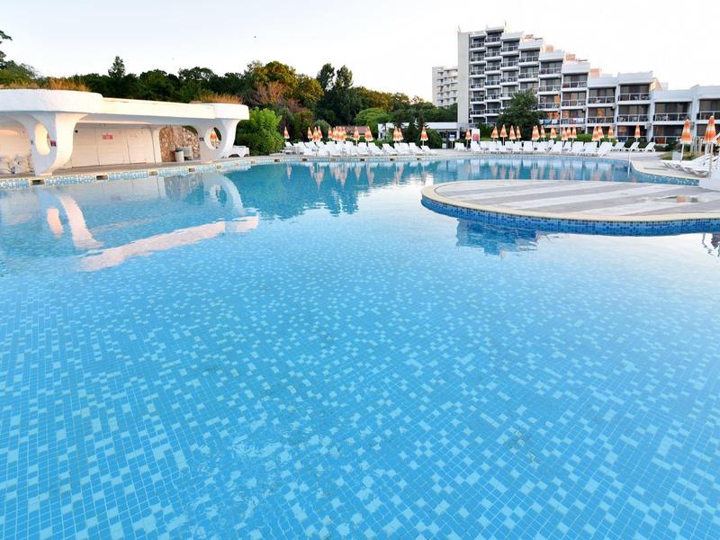 Duży basen hotelowy z leżakami i nowoczesną architekturą w tle pod czystym niebem.