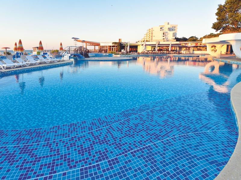 Duży basen z czystą niebieską wodą i leżakami w hotelu o zachodzie słońca.