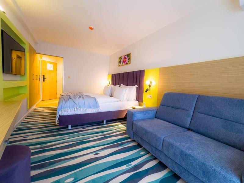 Nowoczesny pokój hotelowy z podwójnym łóżkiem, niebieską sofą i kolorowym dywanem.