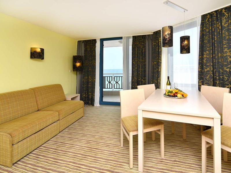 Salon lumineux avec canapé beige, coin repas et balcon avec vue sur la mer.