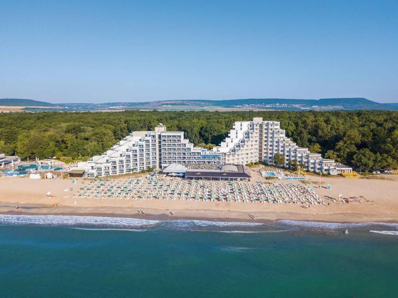 Grand hôtel à deux ailes sur la plage, rangées de parasols et transats devant.