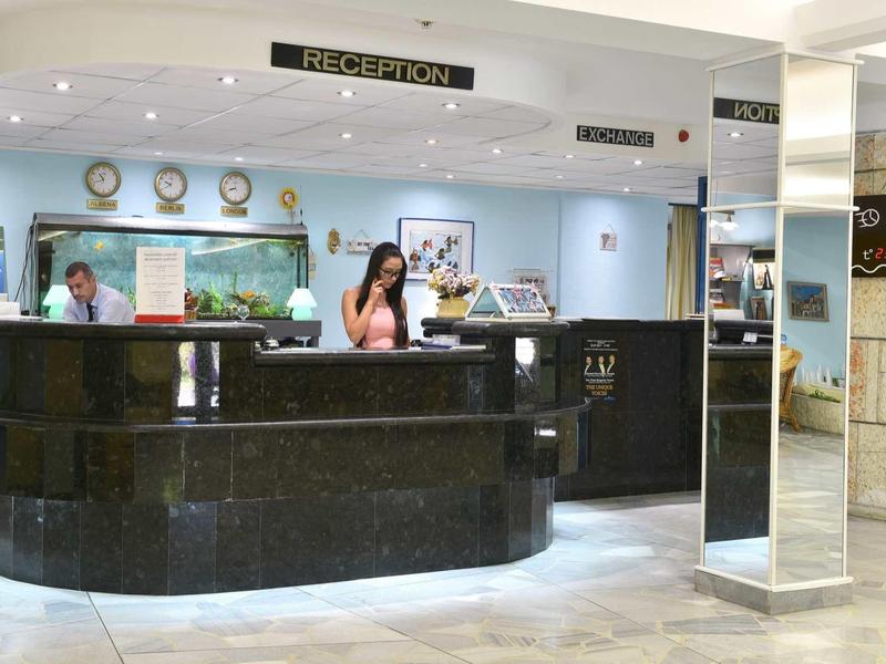 Réception d'hôtel avec comptoir noir et employé en arrière-plan.