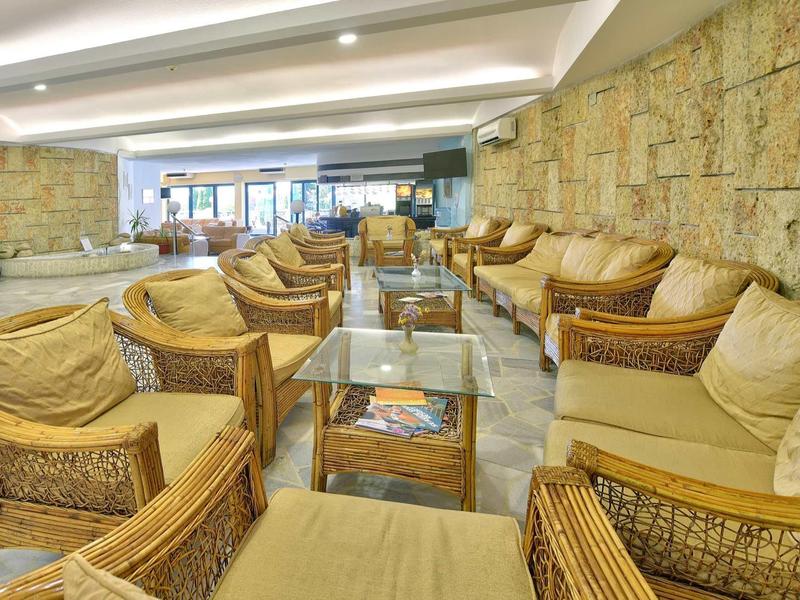 Hall d'hôtel lumineux avec des fauteuils en rotin et des murs en pierre, confortable et accueillant.