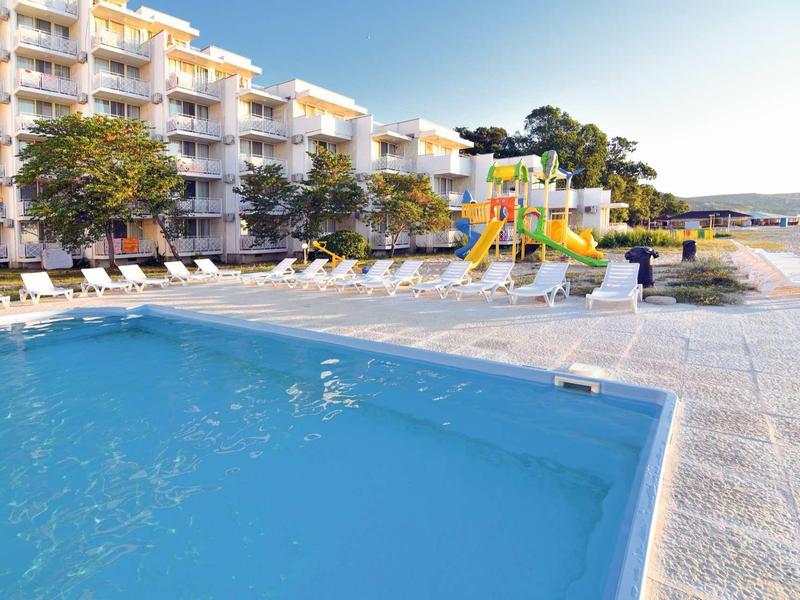 Piscine d'hôtel avec chaises longues et toboggan à côté d'un bâtiment à plusieurs étages sous un ciel clair.
