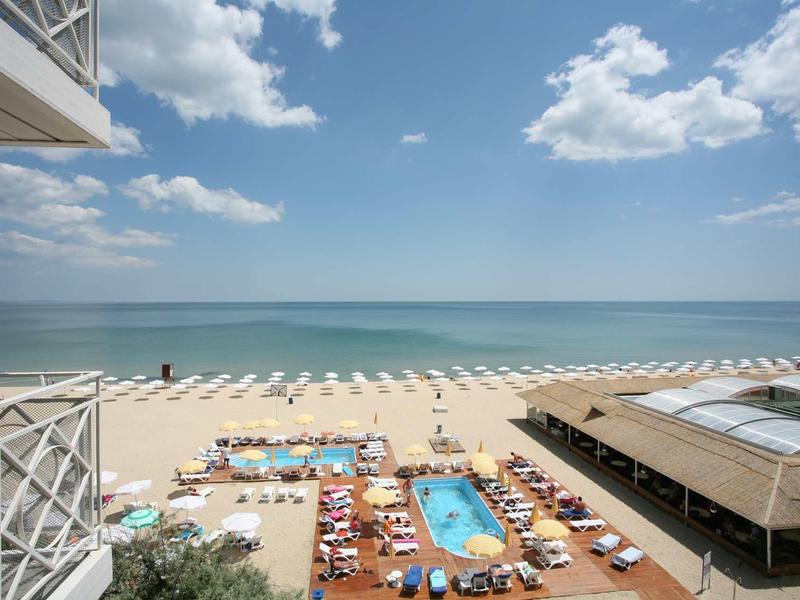 Plage avec transats, piscine et mer bleue sous un ciel partiellement nuageux