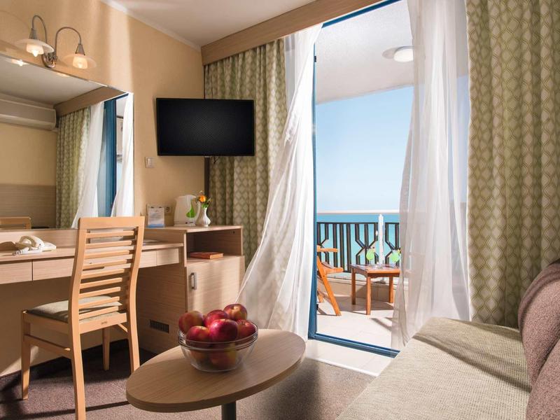 Chambre d'hôtel confortable avec balcon, vue sur la mer, canapé et télévision.