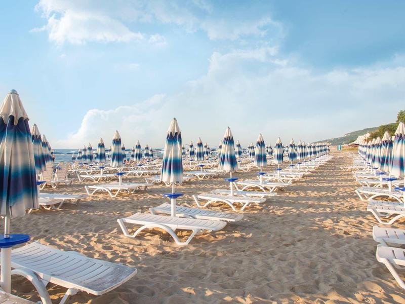 Plage avec rangées de chaises longues et parasols bleus sous un ciel clair.