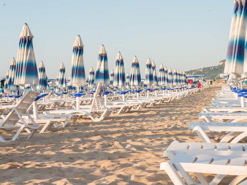 Plage avec de nombreuses chaises longues blanches et des parasols bleus sous un ciel clair.