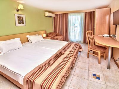 Camera d'hotel luminosa con letto grande, scrivania, sedia, aria condizionata e tende alla finestra.