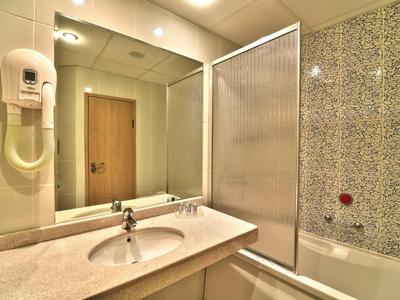 Bagno luminoso con lavandino, specchio, asciugacapelli e vasca con parete doccia