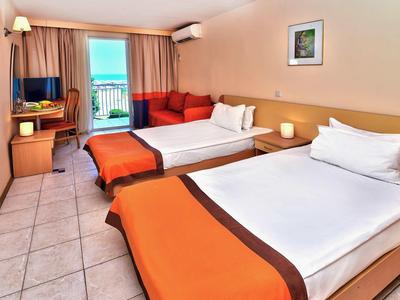 Camera d'hotel con due letti singoli, scrivania, TV e balcone con vista mare.