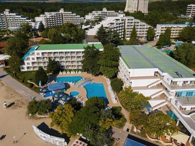 Vista di un hotel con piscina e spiaggia sabbiosa adiacente in un ambiente verde.
