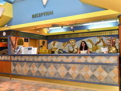 Reception dell'hotel luminosa con piastrelle decorative alle pareti e una donna dietro il bancone.