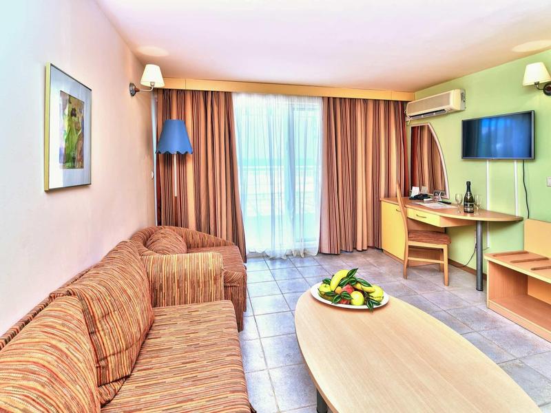 Camera d'hotel luminosa con divano, scrivania, TV e balcone con tende.