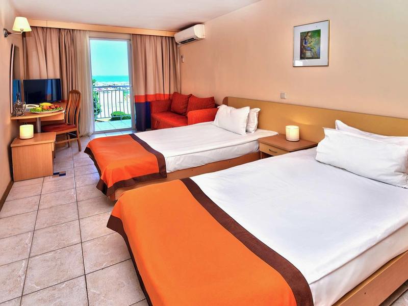 Camera d'hotel con due letti singoli, scrivania, TV e balcone con vista mare.