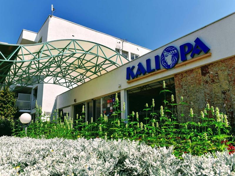 L'hotel Kalimpa con tettoia verde e area esterna curata in una giornata di sole.