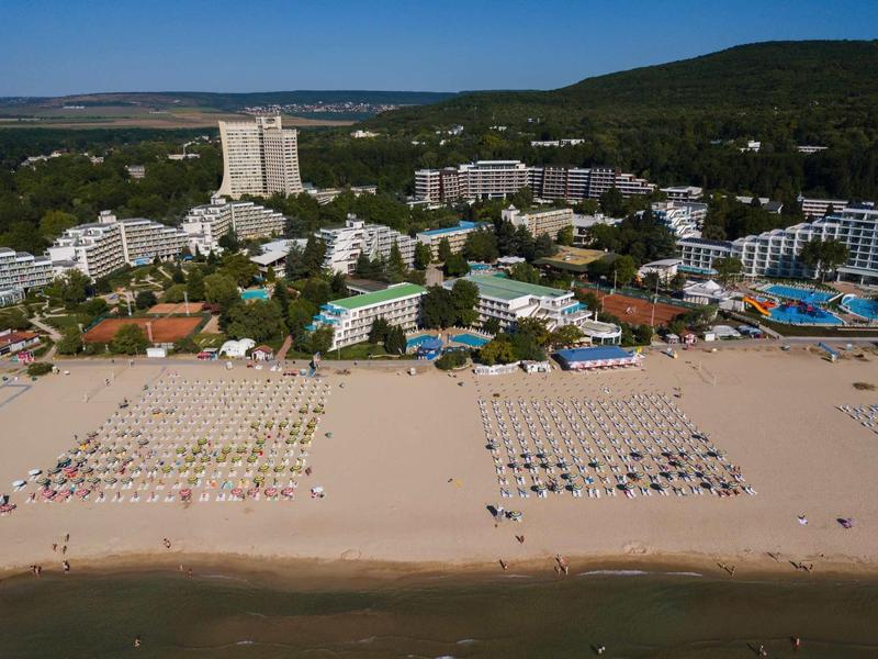 Veduta aerea di un grande resort con spiaggia di sabbia, lettini e foreste circostanti.
