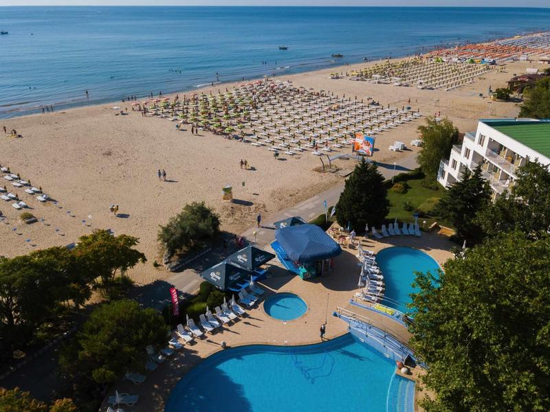 Hotel sulla spiaggia con grande piscina, ombrelloni e ampia spiaggia sabbiosa sul mare.
