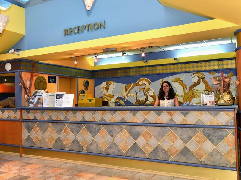 Reception dell'hotel luminosa con piastrelle decorative alle pareti e una donna dietro il bancone.