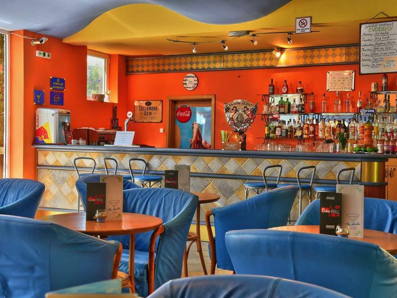 Bar dell'hotel colorata con poltrone blu, tavoli in legno e ampia selezione di bevande dietro il bancone.