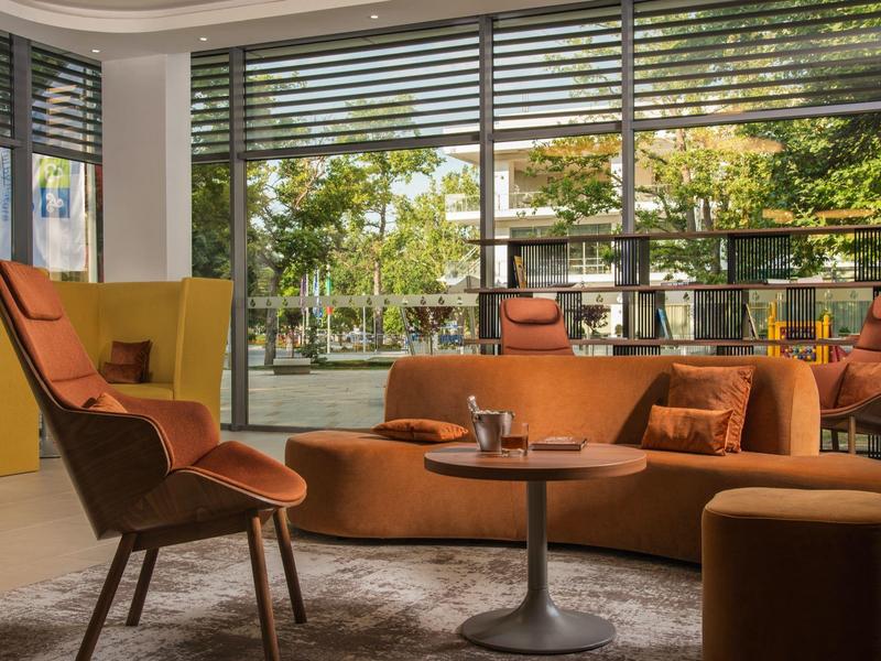 Moderní lounge s oranžovými křesly a velkými okny s výhledem do zahrady.