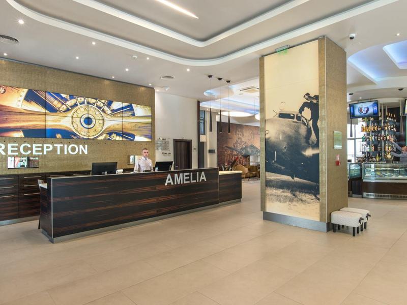 Moderní recepce s velkým pultem a výraznou stěnovou dekorací v světlém hotelu.