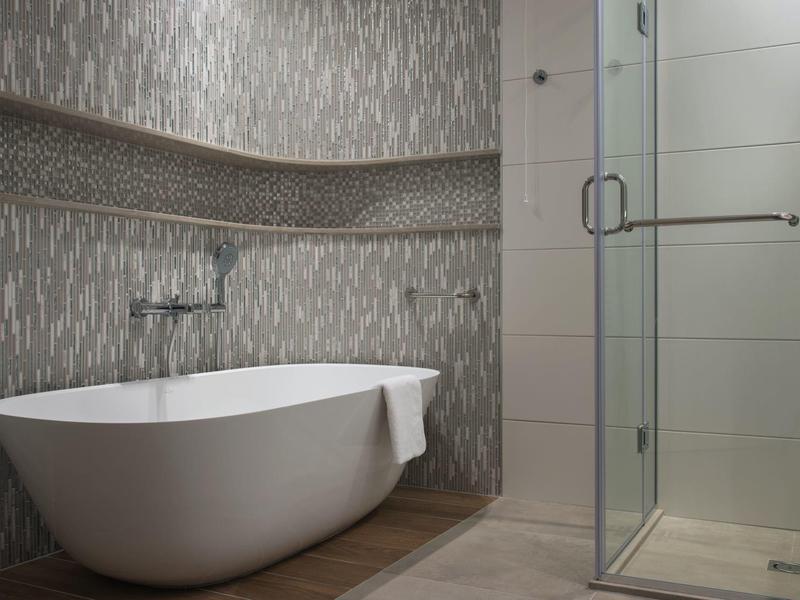 Moderní koupelna s volně stojící vanou a skleněným sprchovým koutem, stěny s elegantními obklady.