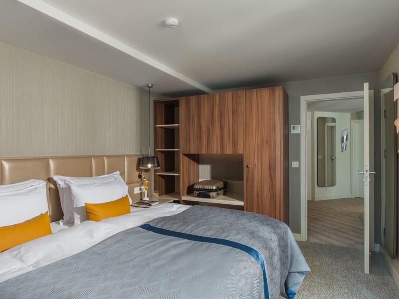 Moderně zařízený hotelový pokoj se dvěma postelemi, šedou přikrývkou a dřevěným nábytkem.