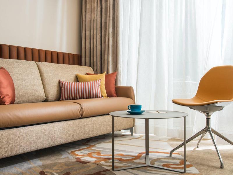 Moderně zařízený obývací pokoj s béžovou pohovkou, barevnými polštáři a žlutou židlí.